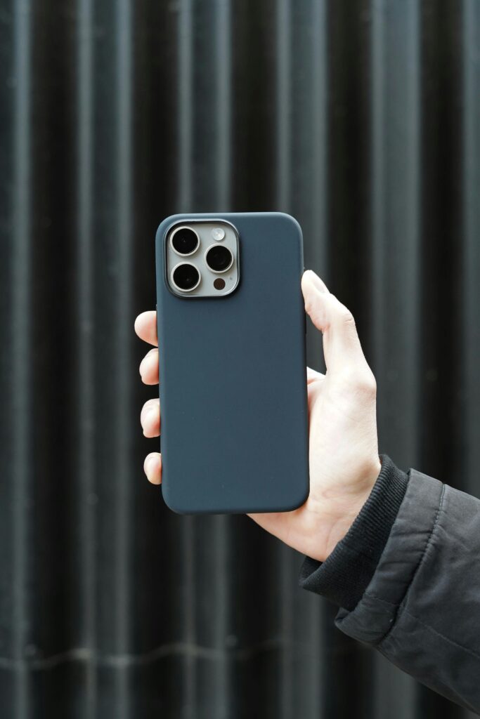 Hand holding a smartphone in a sleek black case against a dark background.